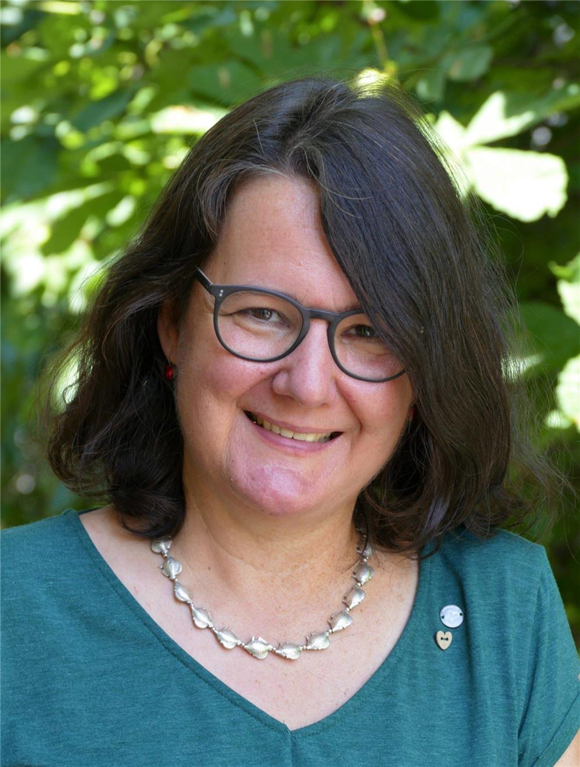 Portraitbild einer brünetten Frau mit Brille und silberfarbener Halskette.