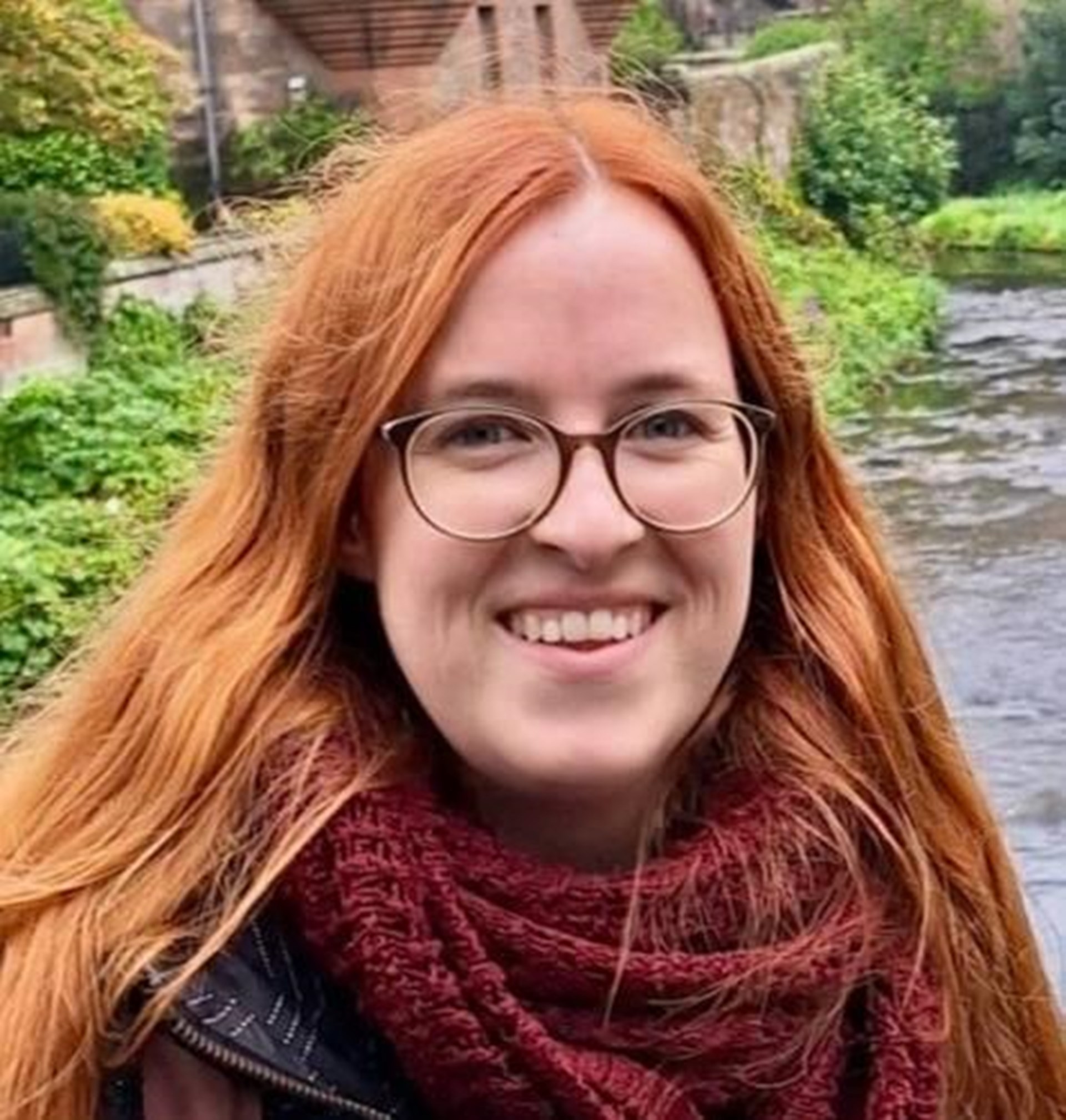 Portrait einer Frau mit langen roten Haaren und Brille.