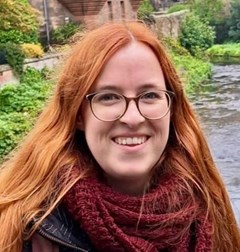 Portrait einer Frau mit langen roten Haaren und Brille.